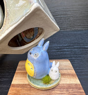 Set of ceramic sculptures, one cube shaped and modeled to look like Totoro. Nearby are a small blue and white chibi Totoro, standing on a small circle platform with a grass tuft.