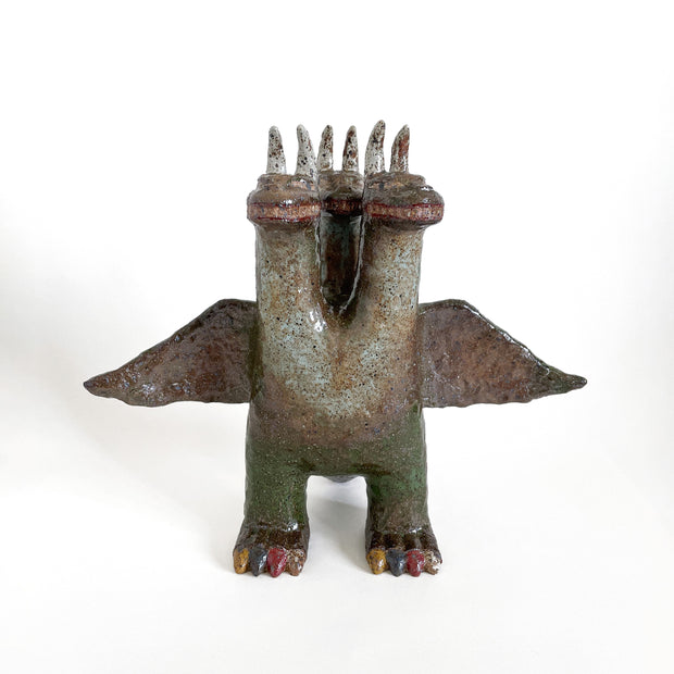 Stoneware sculpture of a 3 headed monster, akin to King Ghidorah. It is earthy green shade with toned down colorful toenails.