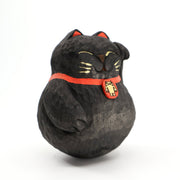 A rounded whittled wooden sculpture of a black maneki cats, smiling with closed eyes and one paw raised. It has gold whiskers and eyelids and wears a red collar with a gold Big Boss Robot on it.
