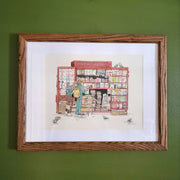 Ink and watercolor illustration of a newstand, with many stacks of magazines and newspapers. 2 people stand facing it, with one reading a magazine and the other reading over their shoulder. Piece is matted into a think wooden frame.