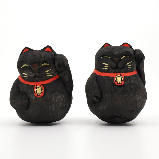 2 rounded whittled wooden sculpture of black maneki cats, smiling with closed eyes and one paw raised. They have gold whiskers and eyelids and wear a red collar with a gold Big Boss Robot on it.