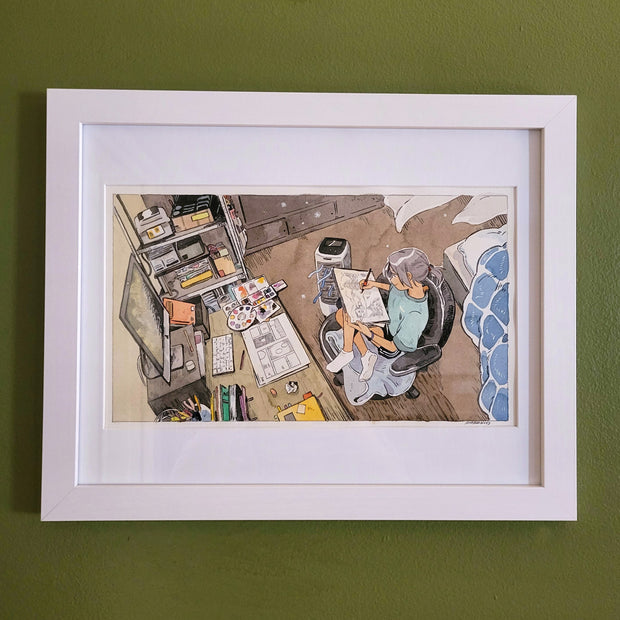  Ink and watercolor drawing of a girl smiling and drawing on a pad of paper. She sits in a desk chair, in front of a desk filled with various art supplies and a drawn comic panel. A floor fan blows air towards the desk. Piece is matted into a white frame.