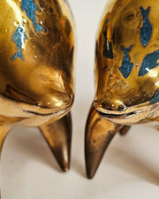 2 gold ceramic sculptures of a rounded body quadruped creature with an open mouth goofy smile. It has blue fish silhouettes swimming on its back.