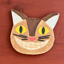 Cat-shaped ceramic coaster with yellow eyes and a pink nose on a wooden surface
