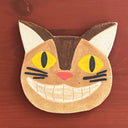Cat-shaped ceramic coaster with yellow eyes and a pink nose on a wooden surface