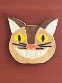 Cat-shaped ceramic coaster with yellow eyes and a pink nose on a wooden surface