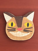 Cat-shaped ceramic coaster with yellow eyes and a pink nose on a wooden surface