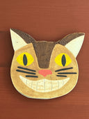 Cat-shaped ceramic coaster with yellow eyes and a pink nose on a wooden surface