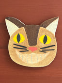 Cat-shaped ceramic coaster with yellow eyes and a pink nose on a wooden surface