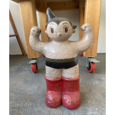 Ceramic sculpture of Astroboy, with his arms up as if flexing his biceps.