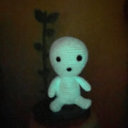 Small crocheted sculpture of a Kodama, a round white forest spirit, glowing in the dark.