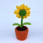 Back view of a crochet sunflower, growing out of a crocheted clay plot with 2 leaves growing from the stem. 