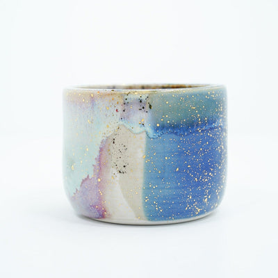 Short ceramic bowl with a blue multicolor glaze and golden splatters.
