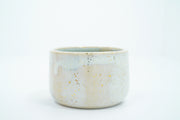 Short ceramic bowl with a light blue and cream multicolor glaze and golden splatters.