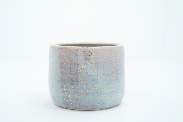 Short ceramic bowl with a light blue and light purple multicolor glaze and golden splatters.