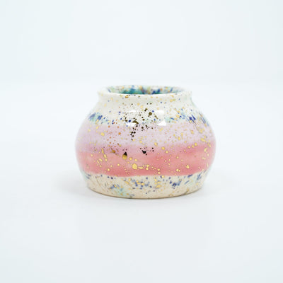 Small ceramic pot, with small opening mostly off white with a light pink stripe running through the middle. Blue and gold speckles decorate the surface.