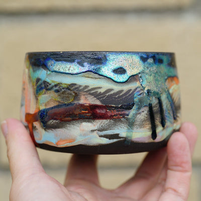 Ceramic pot with many colors and shining elements, looking like an abstract desert landscape.