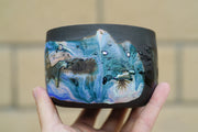 Black ceramic bowl with blue swirled coloring and a shiny abstract design of what looks like a person riding on a horse.