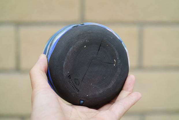 Underside of black ceramic cup with artist's signature stamped into the bottom.