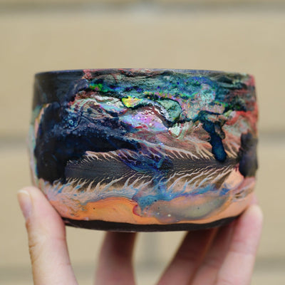 Ceramic pot with many colors and shining elements, looking like an abstract desert landscape.