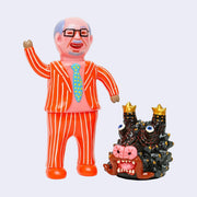 Vinyl figure of a pink man with a balding head and a bright pinstriped business suit. He stands next to a black dragon head with gold color accents. 