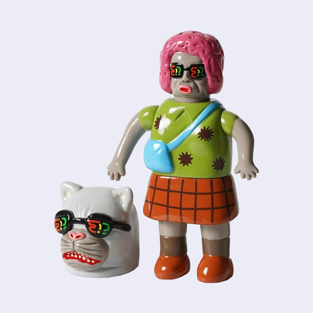 Vinyl figure of a grey woman with a pink short perm and glasses. She wears a crossbody bag and an orange plaid skirt. Near her is a large gray cat head with similar looking sunglasses.