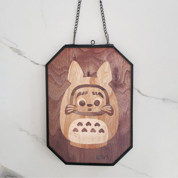 Flat wooden sculpture of a small Daruma, fashioned to look like Totoro. The wood is contained within an open faced wire frame.