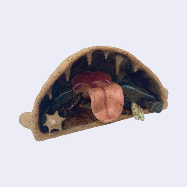 Ceramic sculpture of the interior of a monster's mouth, made to look like an underwater cave. It has a pink tongue and teeth that look like stalactites.