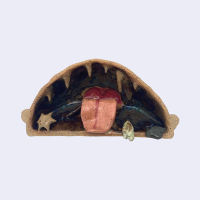 Ceramic sculpture of the interior of a monster's mouth, made to look like an underwater cave. It has a pink tongue and teeth that look like stalactites.   