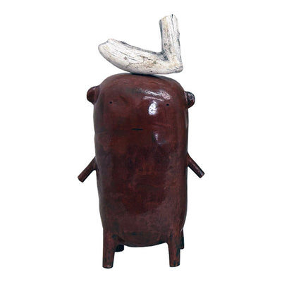 Dark brown ceramic sculpture of a character with small ears and thin arms and legs. It has a piece of wood atop its head.