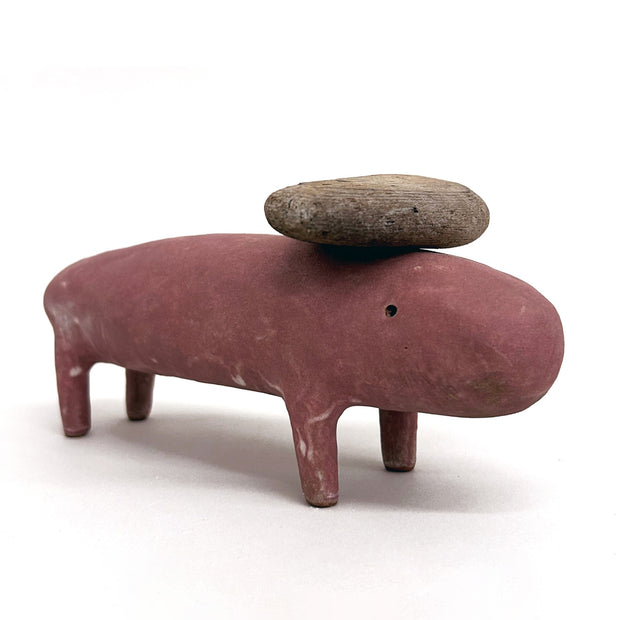 Ceramic sculpture of of a burgundy round animal character with thin short legs and a piece of wood atop its head.