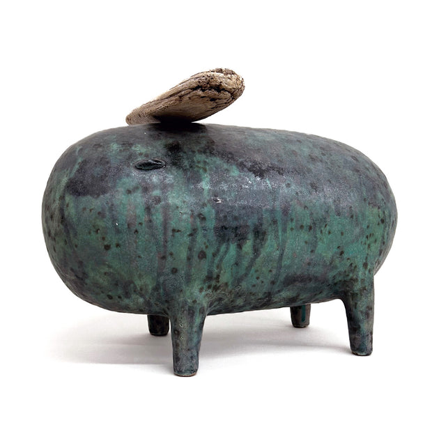 Dark green and black ceramic sculpture of a round bodied animal with 4 small legs and a piece of wood atop its head.