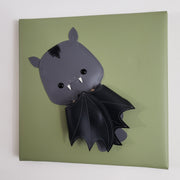 Vinyl canvas flat sculpture of a cartoon style bat, with its wing pulled into its body. It is on a olive green square canvas.
