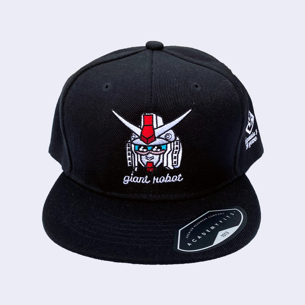 Black cap with an embroidery of a white gundam head with cute kawaii eyes and a smile. Below is "giant robot" written in white lower case cursive.