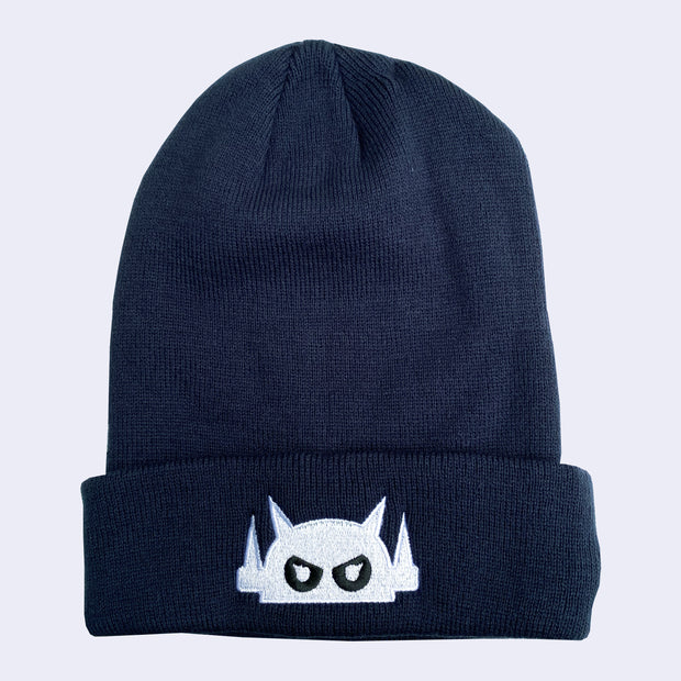 A dark navy blue knit beanie with a robot head stitched on the cuff in white thread, with black eyes.