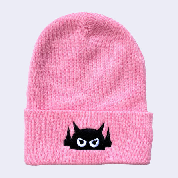 A bright pink knit beanie with robot head stitched on the cuff in black thread, with white eyes.