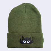 An olive green knit beanie with a robot head stitched on the cuff in black thread, with white eyes.