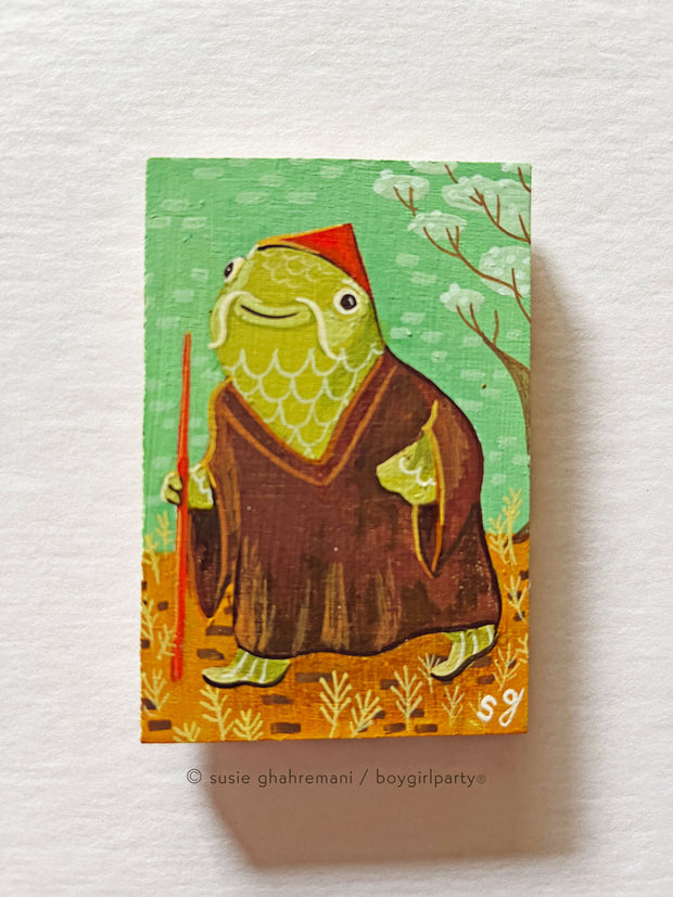 Painting of a fish like creature, with green skin and scales, wearing a brown muumuu and a red cone hat. It holds a walking stick and stands in a yellow field with green background.