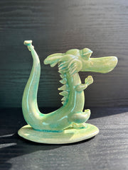 Jade colored ceramic sculpture of a dragon with a large front snout, positioned in a yoga pose with one leg up and its hands at its chest.