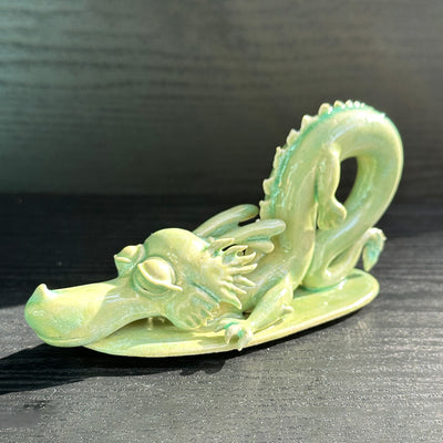 Jade colored ceramic sculpture of a dragon with a large front snout, positioned in the yoga stretch, child's pose. 