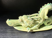 Jade colored ceramic sculpture of a dragon with a large front snout, positioned in the yoga stretch, child's pose.
