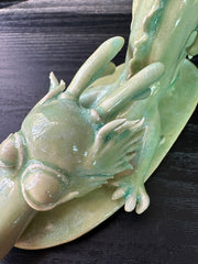 Jade colored ceramic sculpture of a dragon with a large front snout, positioned in the yoga stretch, child's pose.
