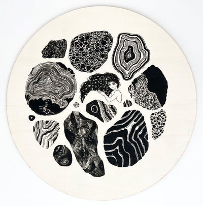 Ink drawing on exposed wooden panel of many geode like designs, all in black and white. In the middle is a woman, only visible from the shoulder up, with long hair that contains a starry sky pattern. Her arm goes over herself like she's laying on her side.