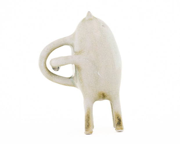 Ceramic sculpture of a light tan character with small ears, eyes and 4 legs. It has curved handle liked shapes overlapping on its back.