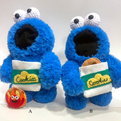 Pair of 2 Cookie Monster plush dolls, with large crocheted eyes. Each has an open mouth and holds a bag of cookies. One side of the cookie shows Elmo, with arms up celebrating the flames behind him.