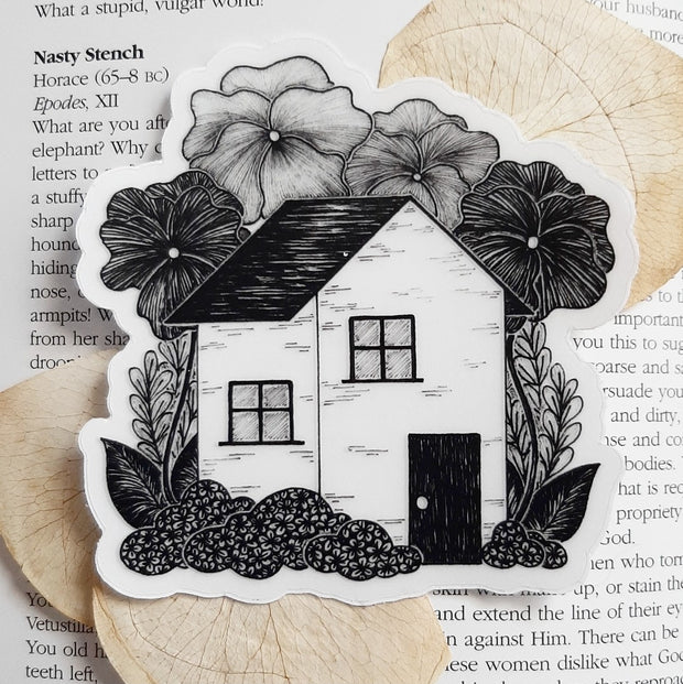 Sticker of a black and white house with very large flowers surrounding it.