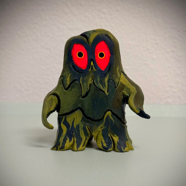 Sculpture of Hedorah, a pollution smoke monster, dark blue and yellowish green. It stands on 2 slimey legs and has large red eyes.
