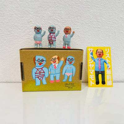Set of 3 small vinyl figures of little business men. One wears a suit, another wears a red bondage wear and the last wears striped underwear. They stand next to a painted box.