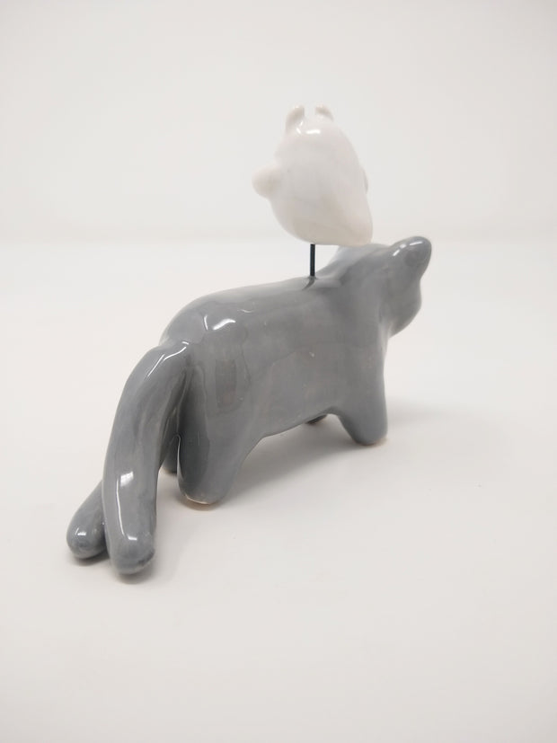 Ceramic sculpture of a gray cat with simplistic body features and a drawn on eyes and whiskers. Hovering atop its back is a small white ghost, with watercolor style tears.