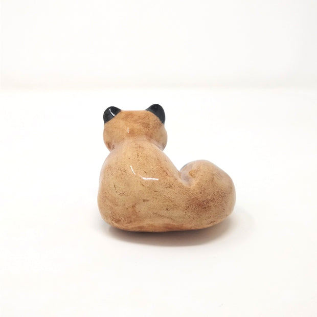 Small ceramic sculpture of a brown fox like creature, with small pointed ears and a large fluffy tail.  Back view.